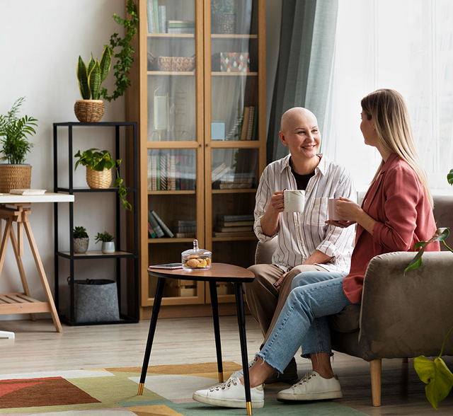 Two people chatting on a sofa in a cozy living room with plants and a coffee table