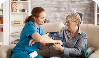 Nurse checking an older patient's blood pressure at home on a couch