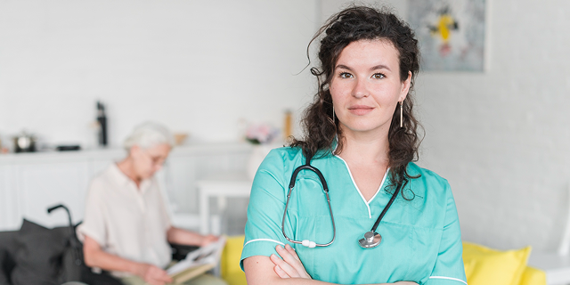 Healthcare worker in teal scrubs with stethoscope, seated in a bright home living room