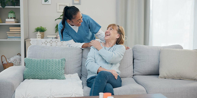 Two women laughing on a light gray couch in a bright living room