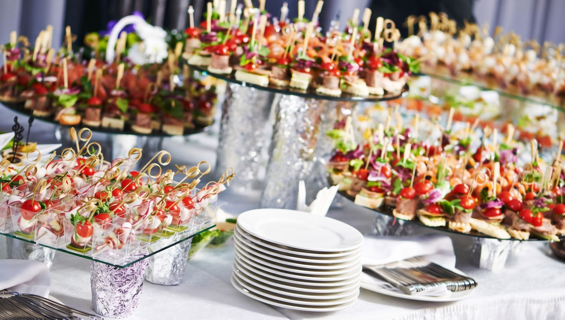 Élégant buffet avec des rangées d'amuse-gueules colorés présentés sur des plateaux en verre et des assiettes empilées à proximité