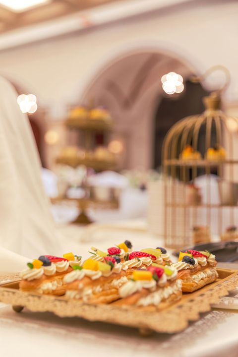 Plateau de pâtisseries garni de fruits et de crème sur un buffet, avec des cages à oiseaux floues en arrière-plan.