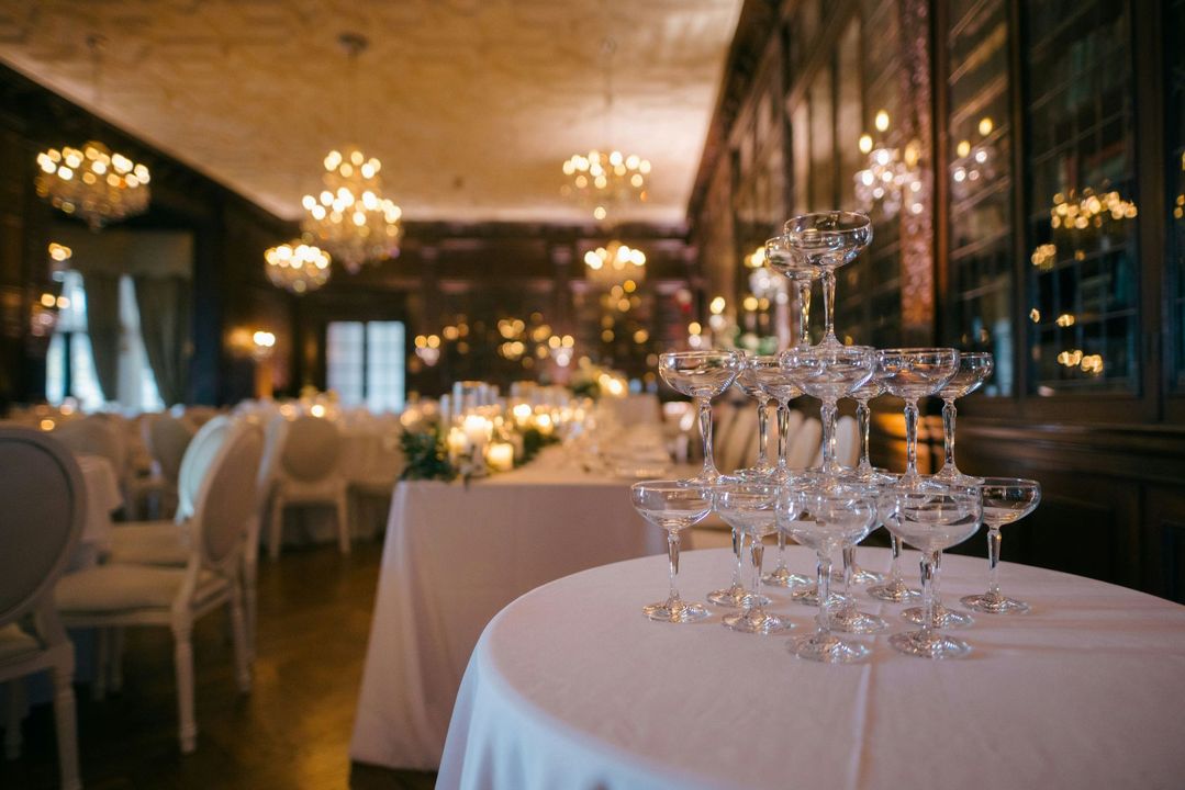 Élégante salle de banquet avec lustres, nappes blanches et verres empilés sur une table à manger