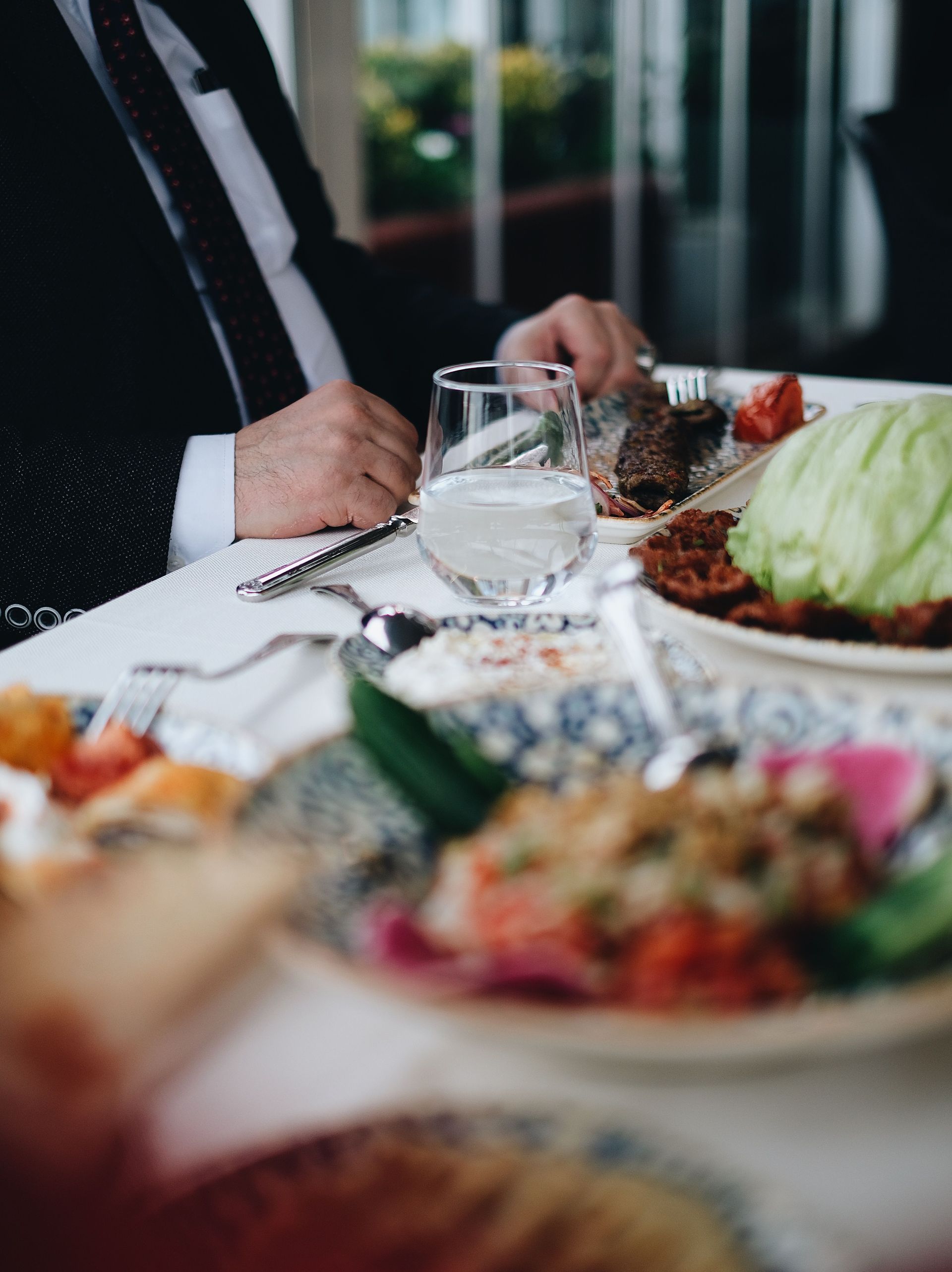 Une personne attablée à un dîner formel, avec des verres à vin, des assiettes et une salade verte au premier plan.