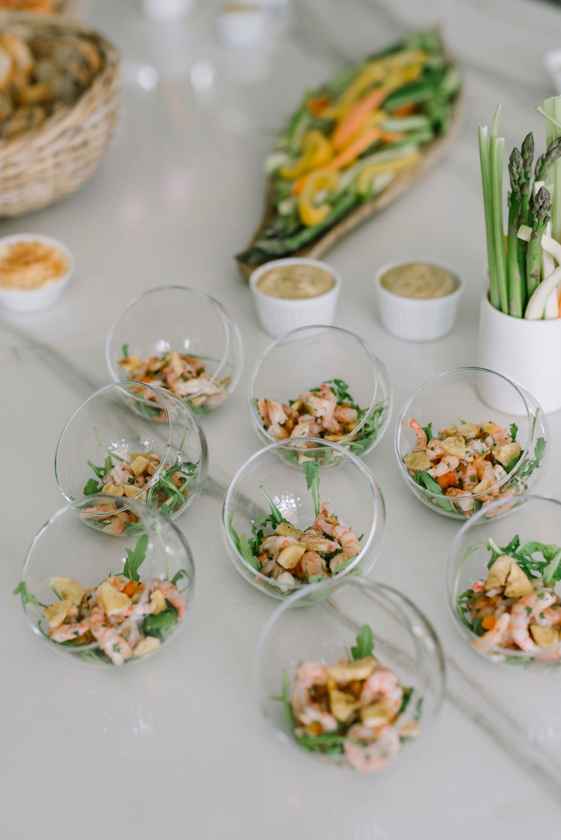 Petits bols d'apéritif disposés sur une table blanche, contenant des légumes frais et des sauces pour trempette, pour un service traiteur.