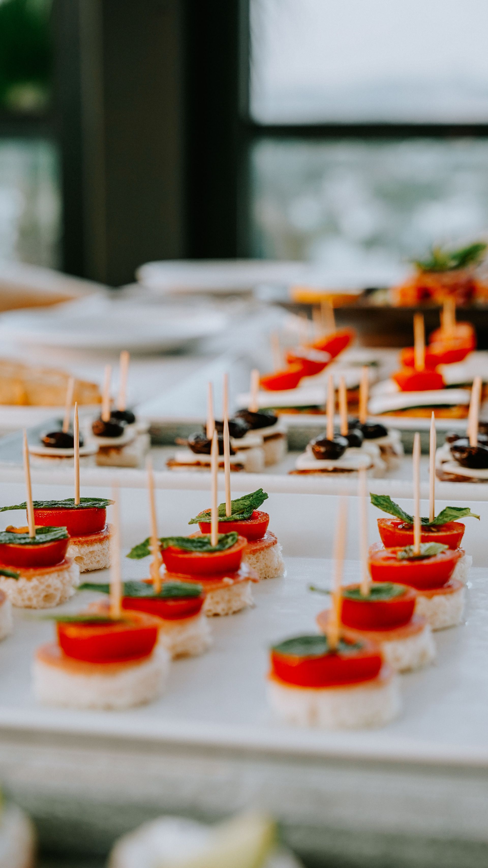 Assortiment de bouchées apéritives présentées sur des plateaux blancs, sur une table de buffet, garnies de décorations rouges.