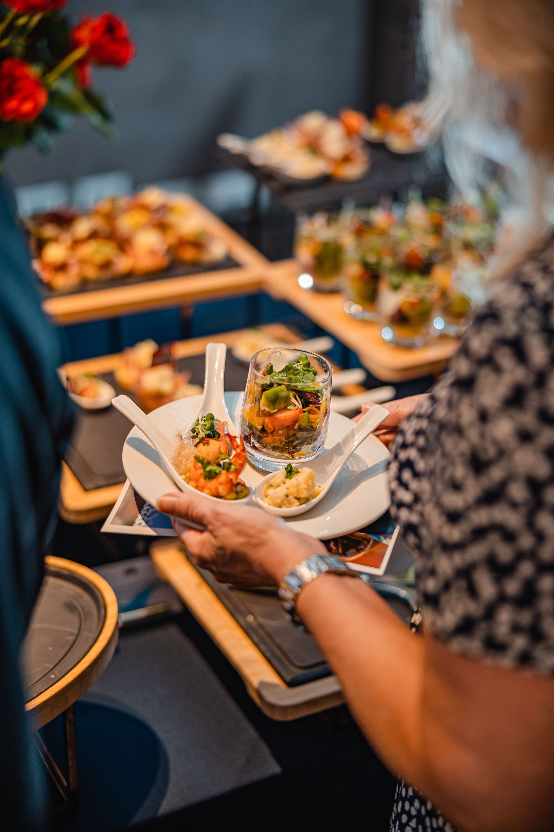 Une personne tenant une assiette d'amuse-bouche devant un buffet garni de plateaux de plats colorés.