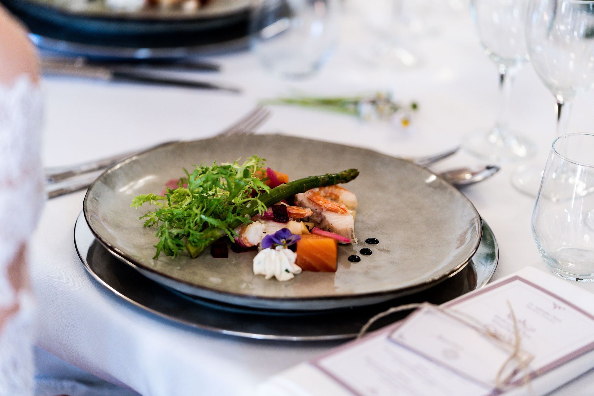 Plat gastronomique élégamment présenté sur une table à manger, composé de verdure, de légumes et de sauce noire.