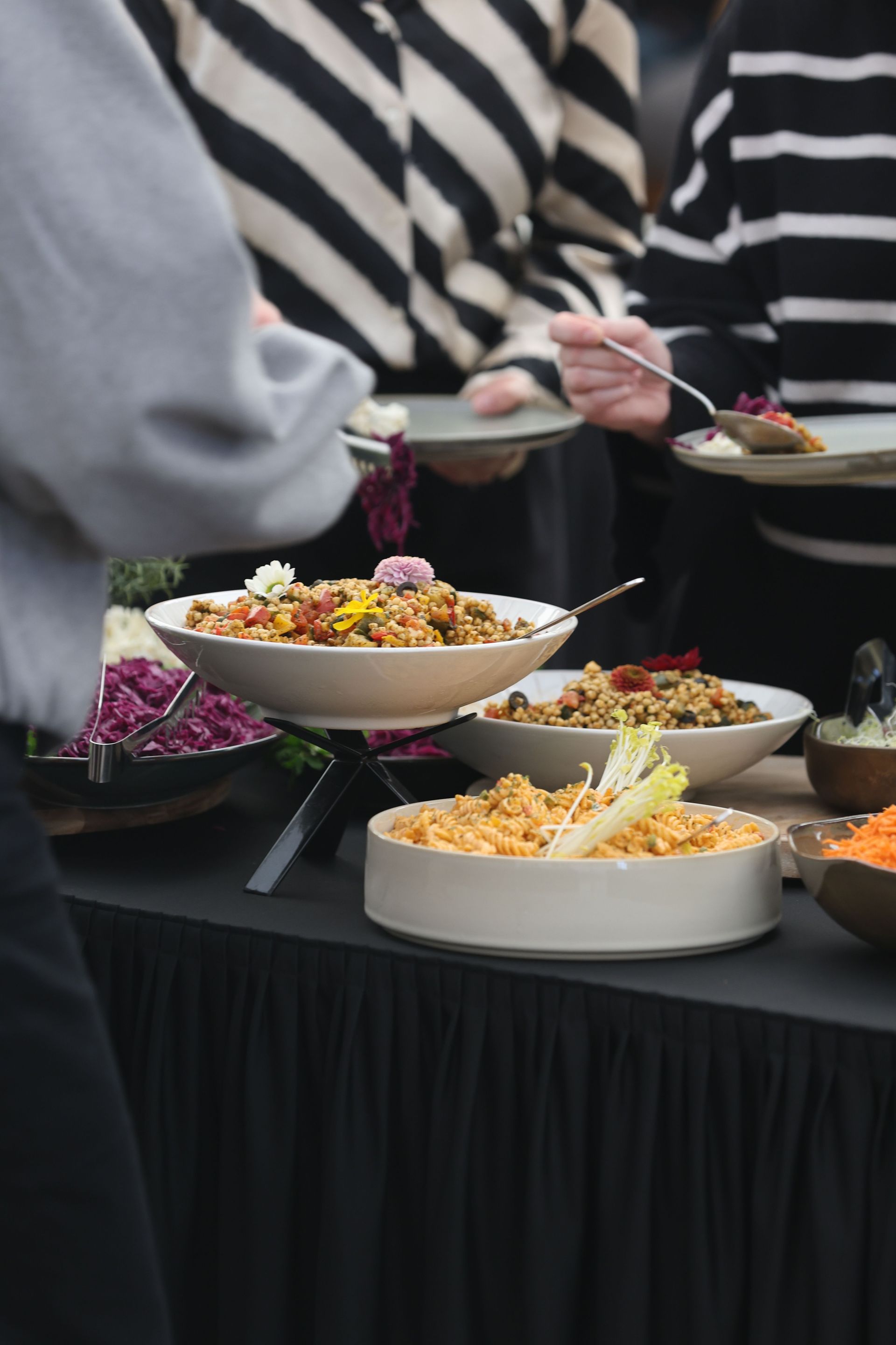 Un buffet avec plusieurs saladiers colorés servis par des personnes en hauts rayés.