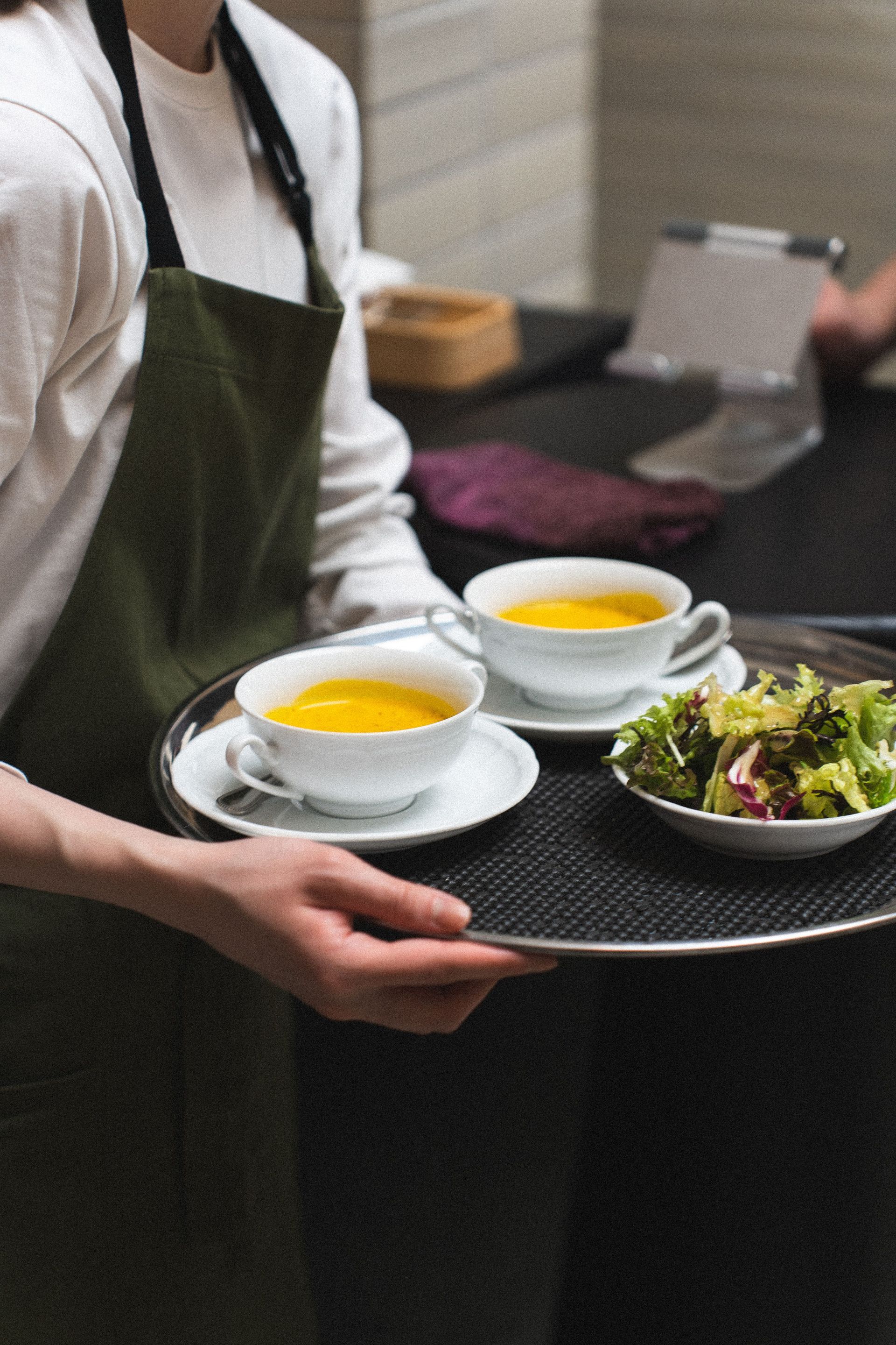 Serveuse portant un plateau avec deux bols de soupe et une salade d'accompagnement dans un restaurant