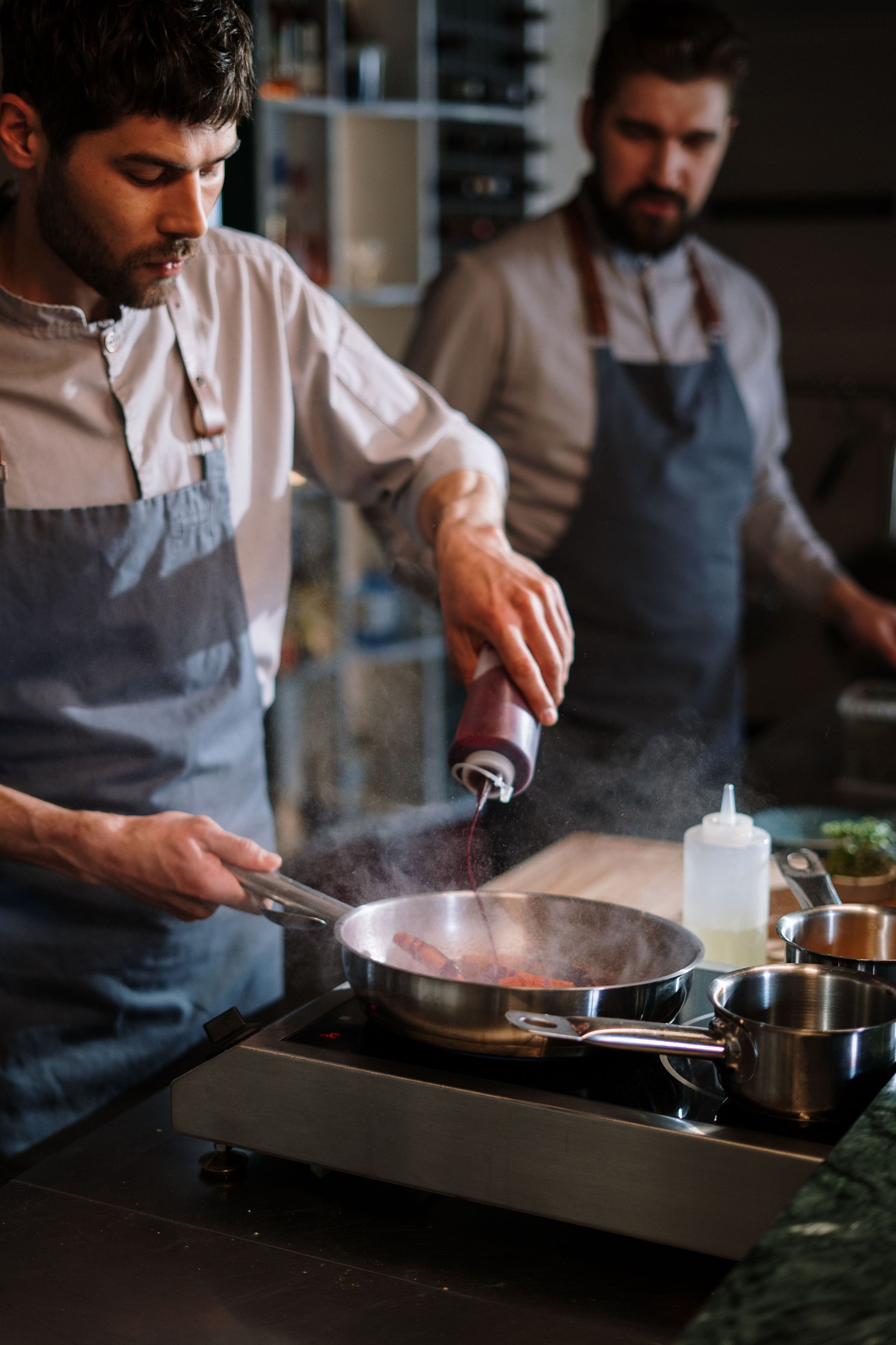 Un chef assaisonne une poêle tandis qu'un autre travaille à proximité dans une cuisine professionnelle