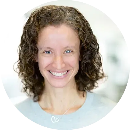 Woman with curly brown hair smiles at the camera, wearing a light blue shirt.