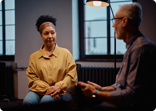 Woman in yellow shirt and man in blue shirt sit facing each other in a room, conversing.
