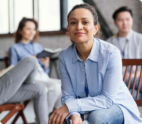 Woman smiling in a blue shirt, seated with others in a workshop setting.