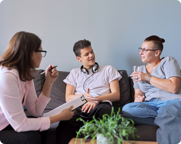 Therapist with pen and notepad speaks to two people on a couch.