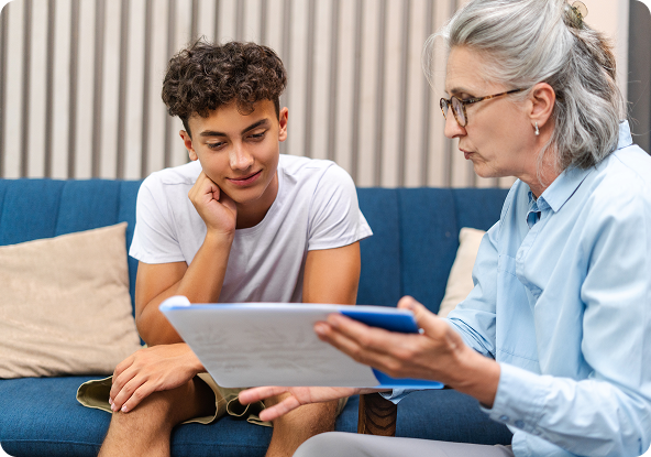 Teenager and therapist looking at documents on a blue couch in a room.