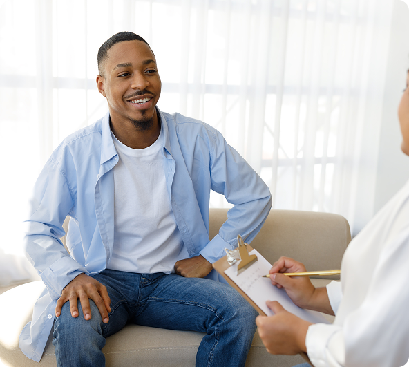 Man in a blue shirt smiling, talking to a person holding a clipboard in an office setting.