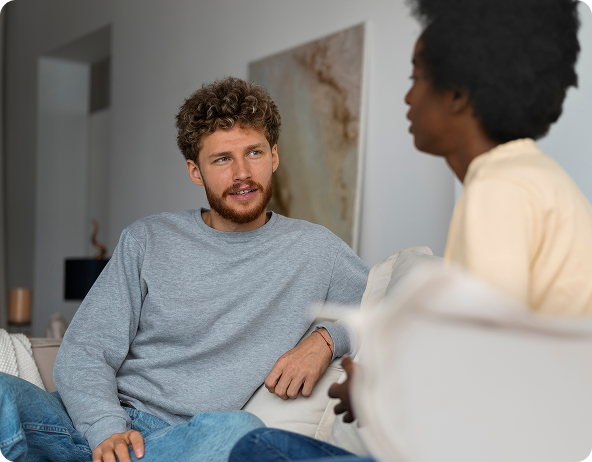 Man with curly hair in gray shirt talking to person in light yellow shirt.