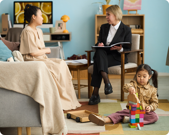 Woman and therapist in an office setting; child plays with blocks on the floor.