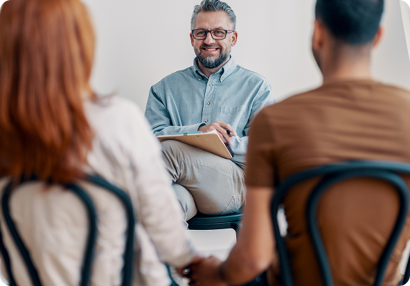 Couple holding hands in couples therapy session with counselor smiling.