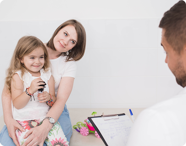 Woman holding child, at doctor's office. Doctor facing them, holding clipboard.