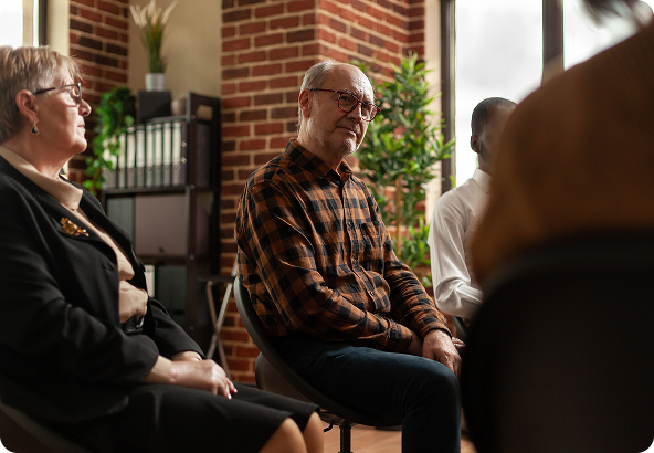 People sitting in a circle in a room; the man in the center looks contemplative.