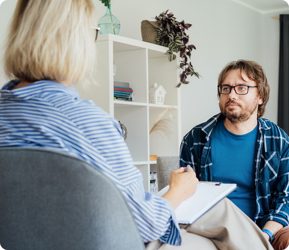 Therapist with notepad listens to a man in a counseling session.