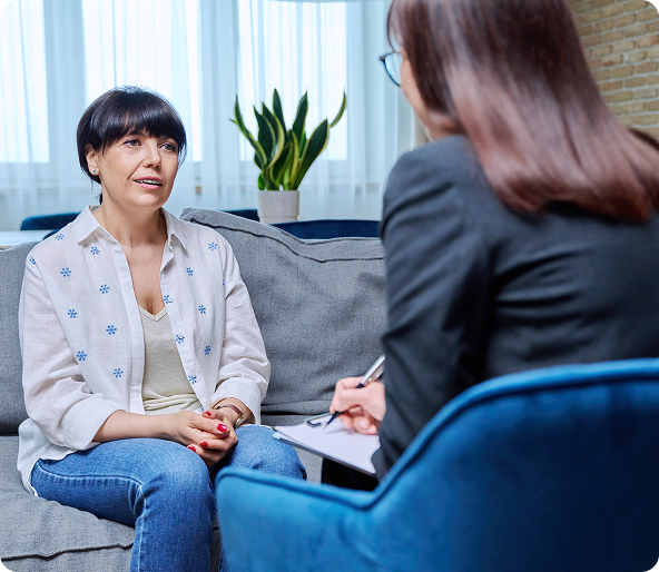 Woman in a therapy session talking to a person taking notes. They are seated in a living room.