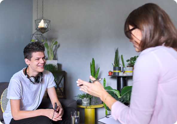 A young person smiles during a session with a therapist, who gestures and holds a pen.