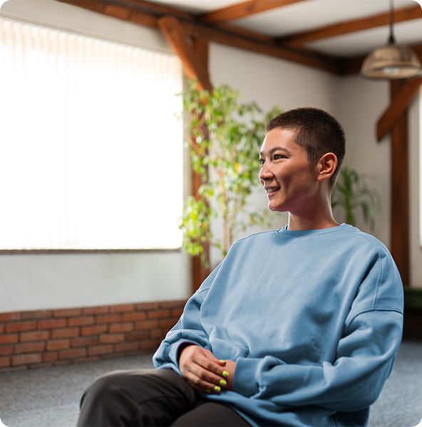 Woman with a buzz cut smiling, wearing a blue sweater, sitting indoors, bright room.