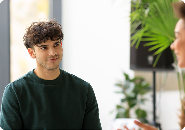 Man in green shirt smiles at person out of frame, indoor setting.