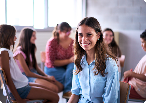 Woman smiles at camera, in a circle with others. They are in a room with a window.