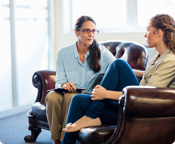 Woman in glasses speaks to another woman in an office setting.