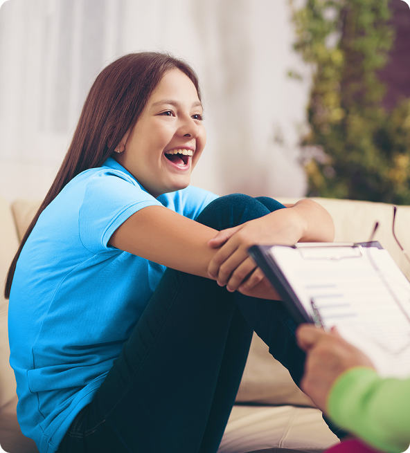 Teenager laughing during a therapy session; seated on a couch, holding clipboard.