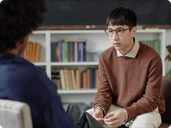 Man in glasses talking to another person in a therapy session; bookshelves in the background.