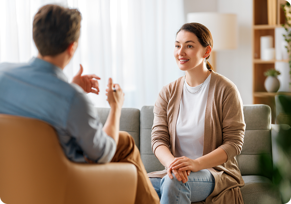 Woman sitting on a couch smiling while talking to a man in a counseling session.