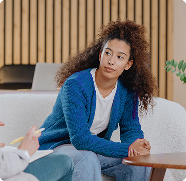 Woman in blue sweater sits, listening attentively, in a therapy session.