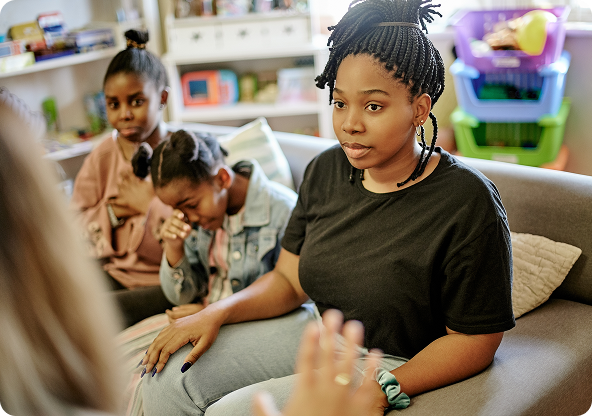 Woman on a couch with two children listening. Indoors, neutral colors, serious expressions.
