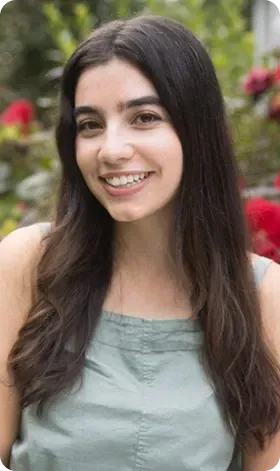 Smiling woman with long dark hair, wearing a green top, in a garden setting.