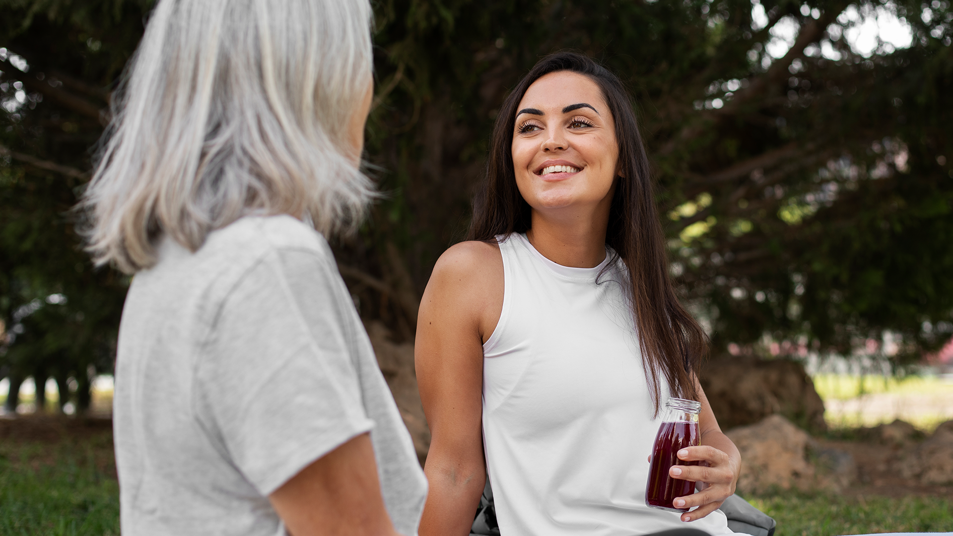 Two women talking outdoors, one smiling and holding a drink