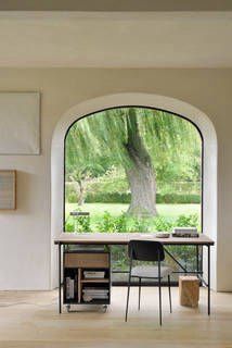 Ein Schreibtisch und ein Stuhl vor einem großen Fenster mit Blick auf einen Baum.