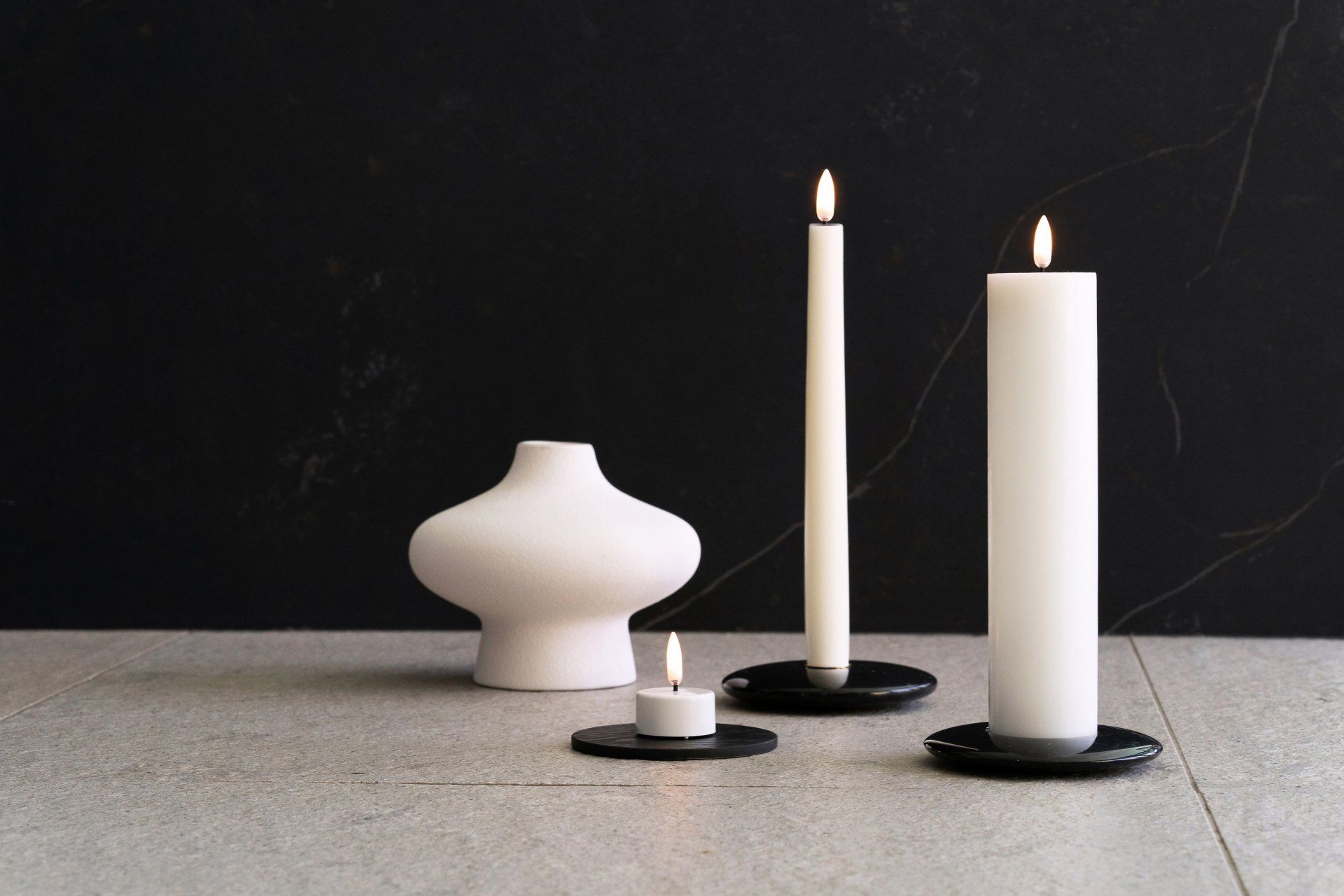 Drei Kerzen und eine Vase auf einem Tisch mit schwarzem Hintergrund