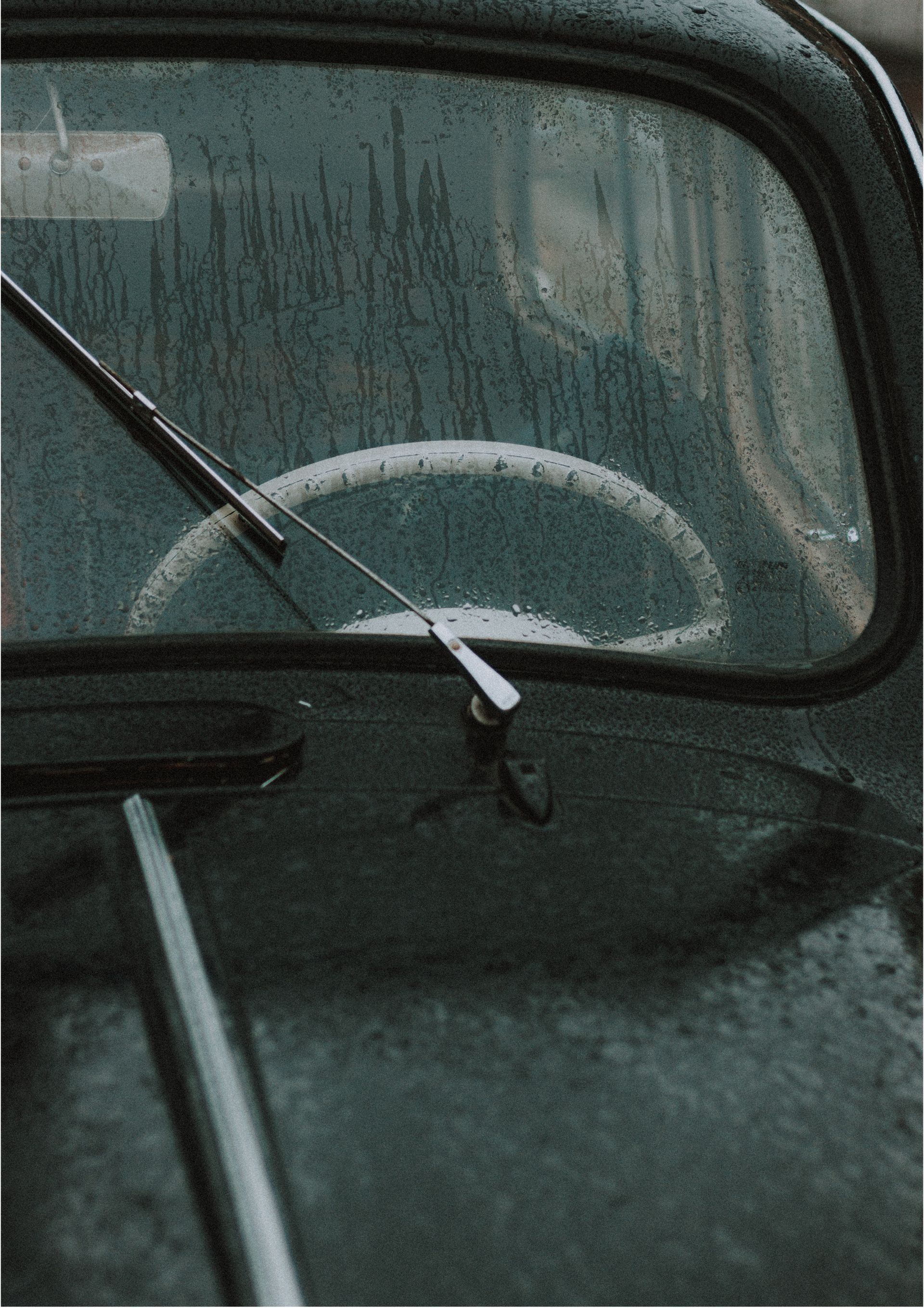 Rain-speckled car window with a windshield wiper and a blurred side mirror view