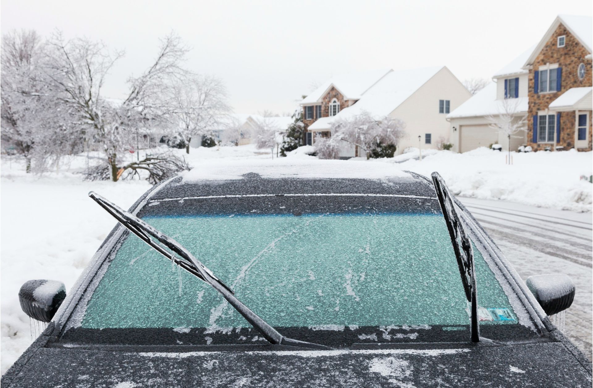 Snow-covered car windshield with wipers up in a snowy suburban neighborhood