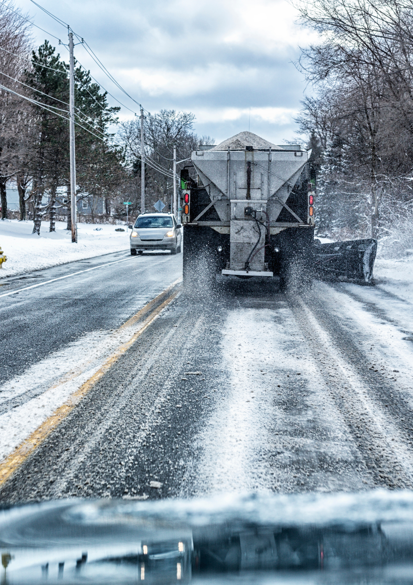 Snowy road behind a salt truck with a car approaching on an icy winter street