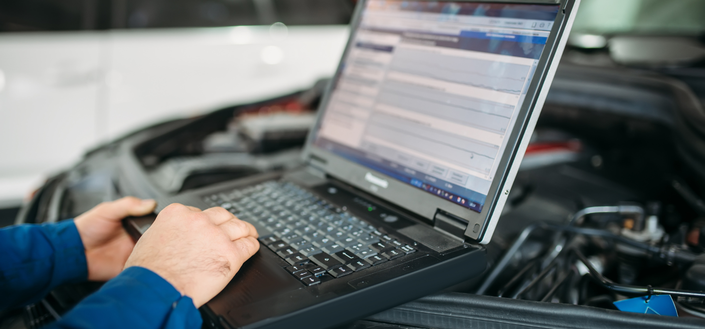 Mechanic using a laptop to diagnose a car engine in a garage
