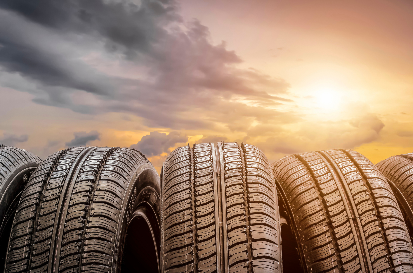 Rows of car tires in a lot at sunset, with dramatic clouds and warm golden light