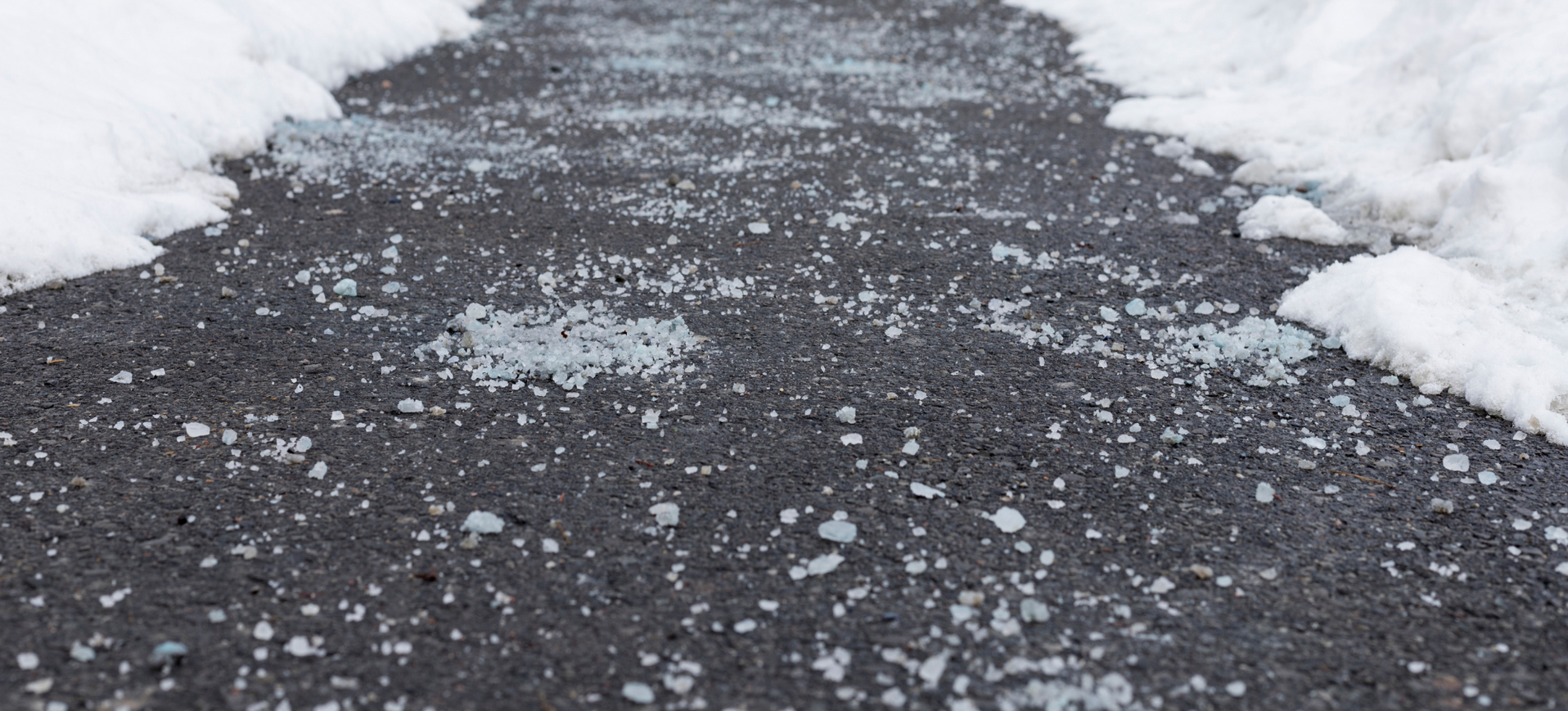 Snow-covered asphalt path with patches of exposed pavement and scattered ice