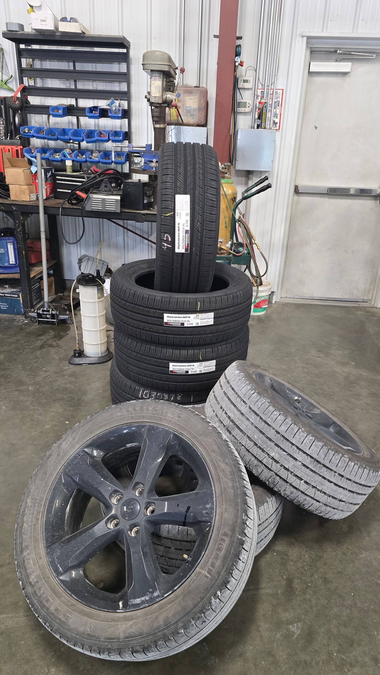 Stack of tires in a garage, with several loose tires and a mounted wheel in the foreground.