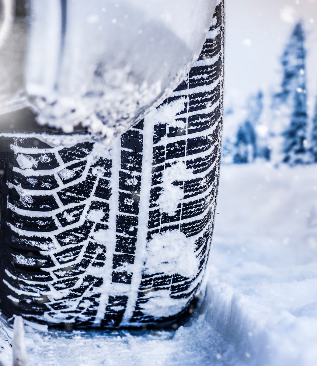 Close-up of a snow-covered car tire with deep tread in a snowy winter scene